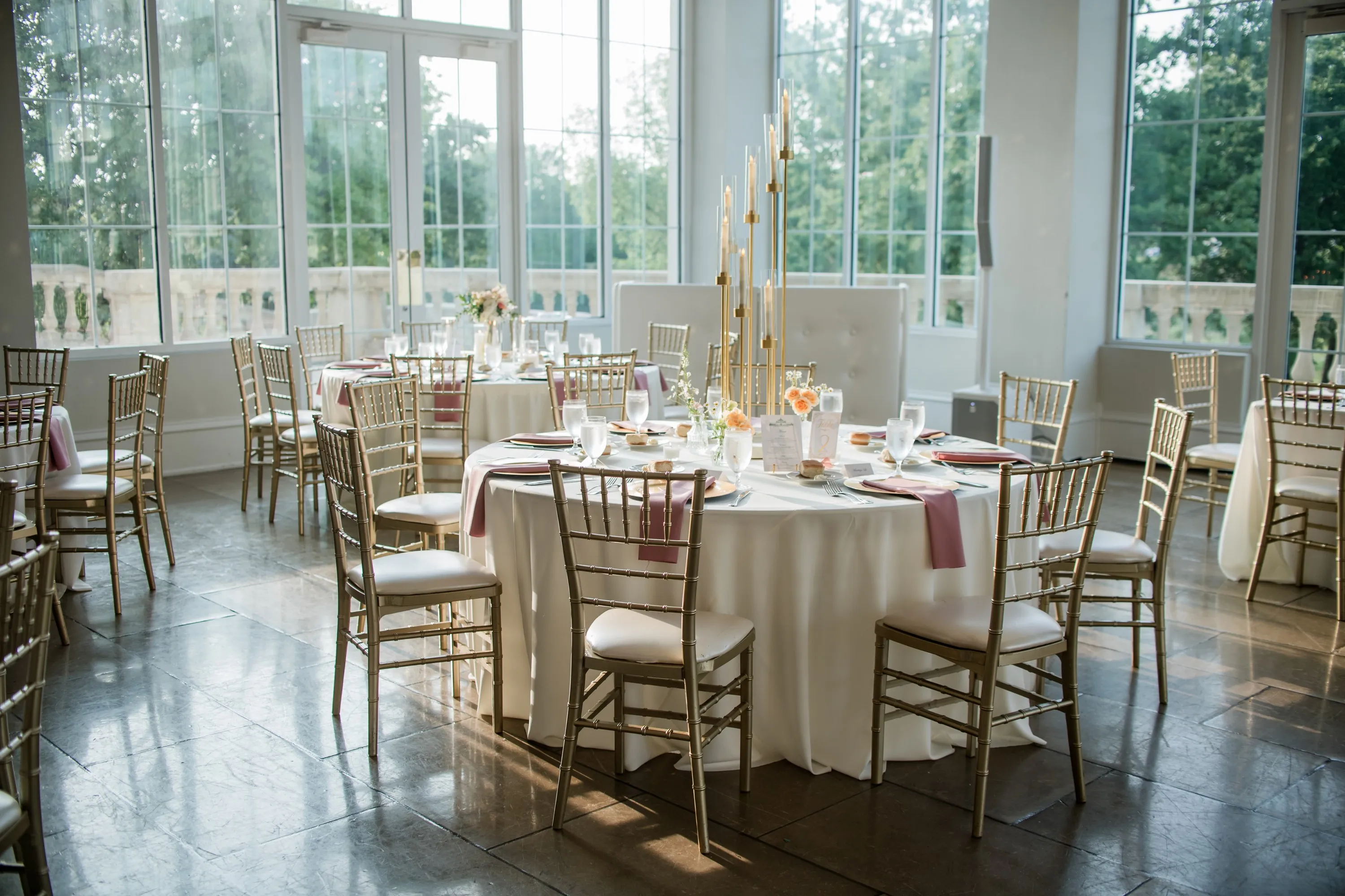 A reception room set with round tables and gold candelabras