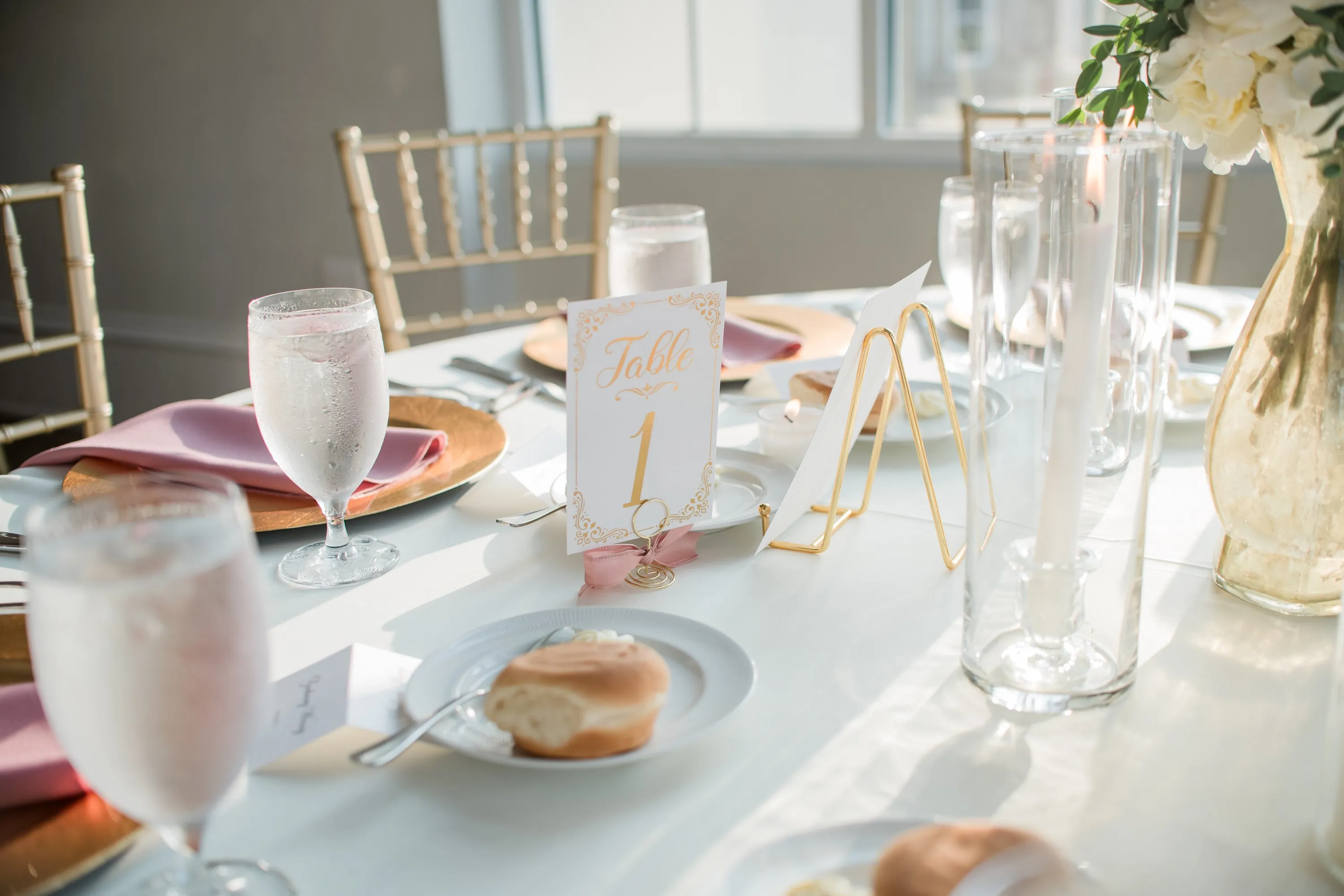 A place setting with gold charger, blush napkin and taper candles